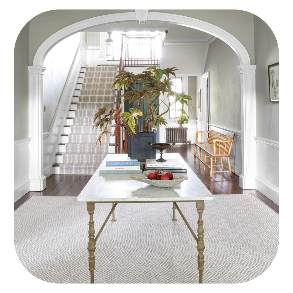 Custom carpeted staircase in a home's foyer with a big area rug. Carpet is white and beige.