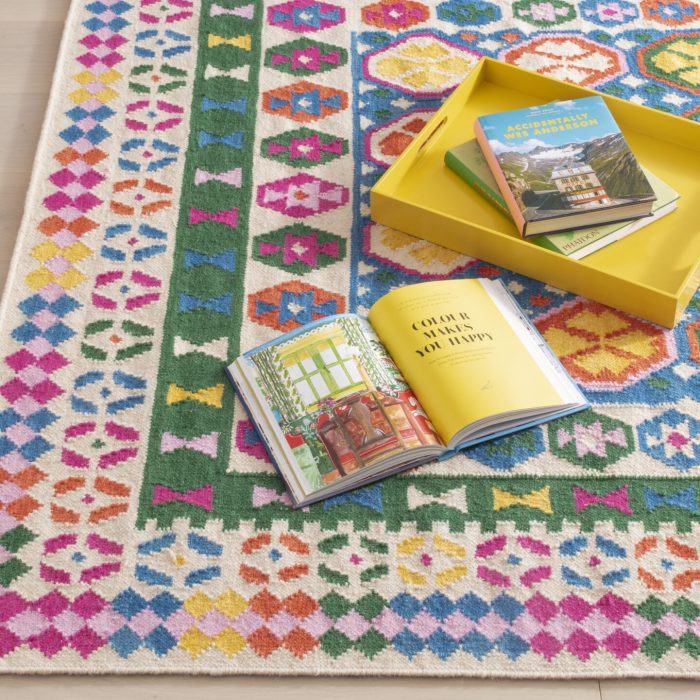 Albert and Dash multicolored indoor rug with bright pink, yellow, orange, blue, and green pattern with a bright yellow breakfast tray and books on top.