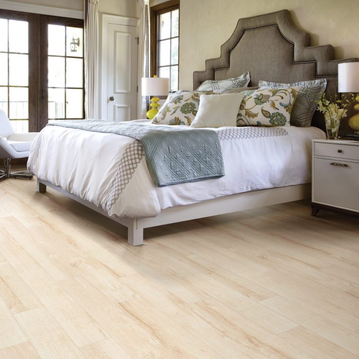 Bedroom with white bedding and light brown laminate flooring